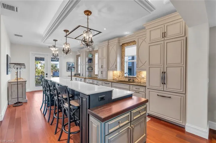 Kitchen with cream cabinets, a kitchen island with sink, a kitchen breakfast bar, decorative light fixtures, and tasteful backsplash