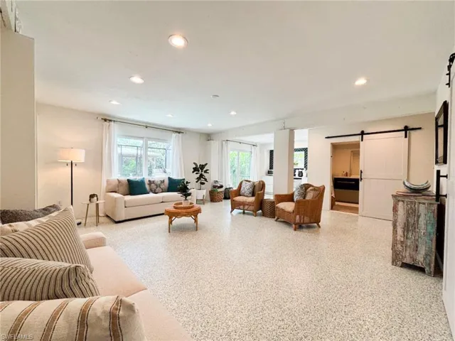 Living room with a barn door, recessed lighting, and dark aggregate flooring