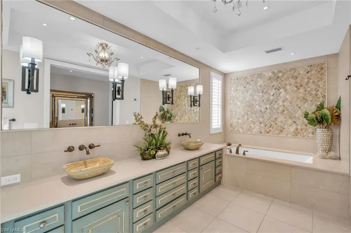 Bathroom featuring a raised ceiling, double vanity, a bath, light tile patterned floors, and a chandelier