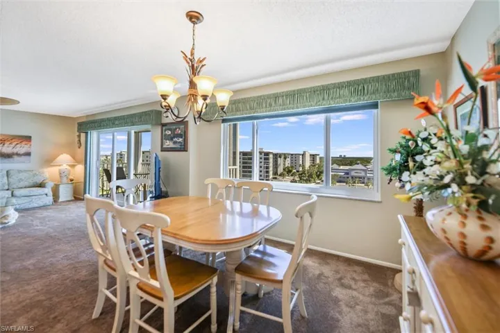 Dining room featuring healthy amount of natural light, dark colored carpet, a chandelier, and a textured ceiling