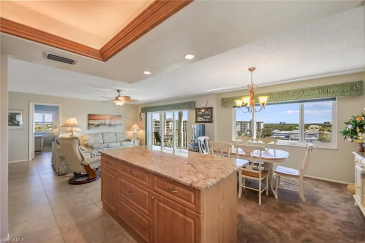 Kitchen with light stone countertops, brown cabinets, a center island, a ceiling fan, and pendant lighting