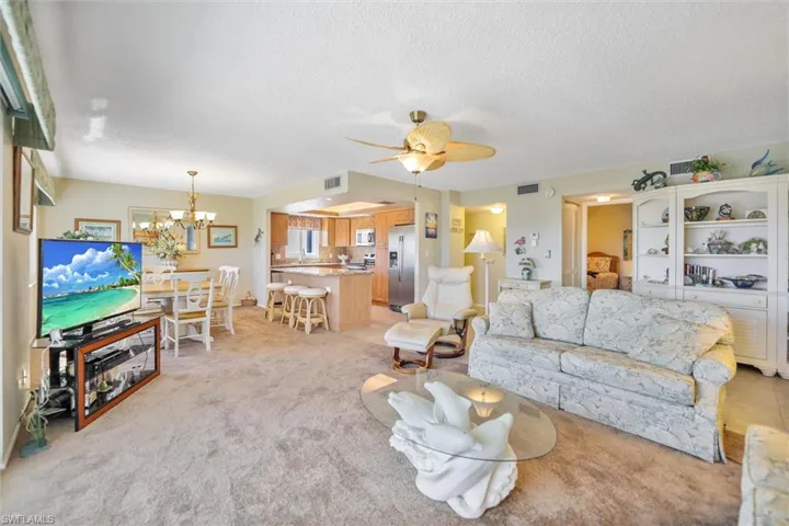 Living area featuring light colored carpet, a ceiling fan, a textured ceiling, and a chandelier