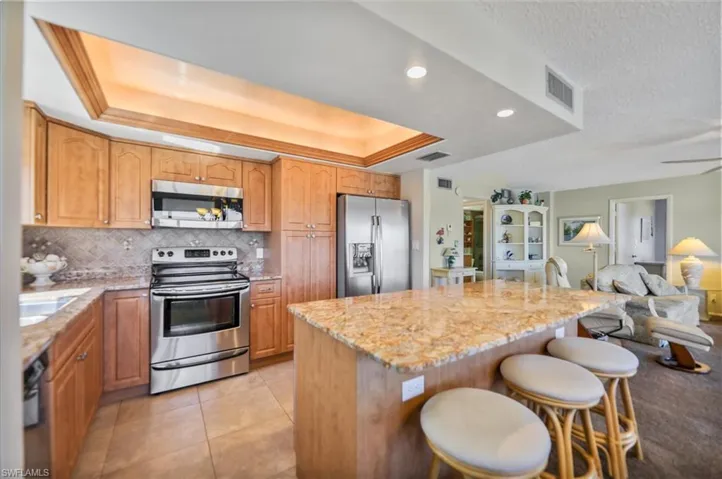 Kitchen featuring stainless steel appliances, open floor plan, a breakfast bar, light stone counters, and recessed lighting
