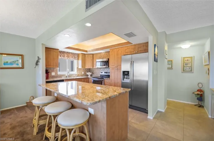 Kitchen featuring stainless steel appliances, light stone counters, backsplash, a tray ceiling, and a kitchen breakfast bar
