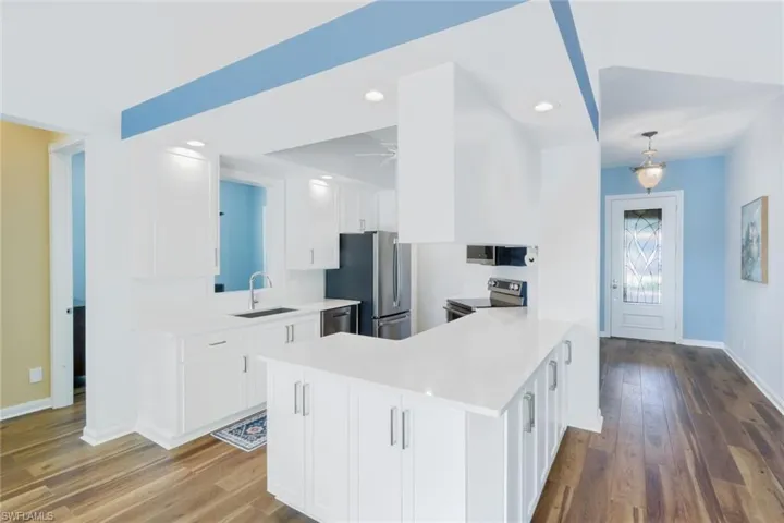 Kitchen featuring white cabinetry, a peninsula, stainless steel appliances, dark wood finished floors, and recessed lighting