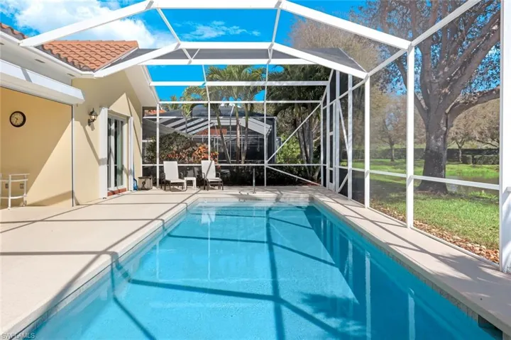 Outdoor pool with a sunroom, a patio area, glass enclosure, and a lawn