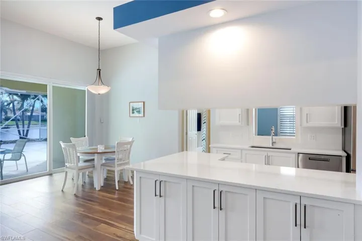 Kitchen featuring white cabinets, dishwasher, dark wood-style floors, light stone counters, and decorative light fixtures