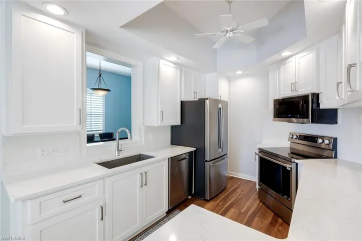 Kitchen featuring stainless steel appliances, dark wood-style floors, white cabinets, recessed lighting, and light stone countertops
