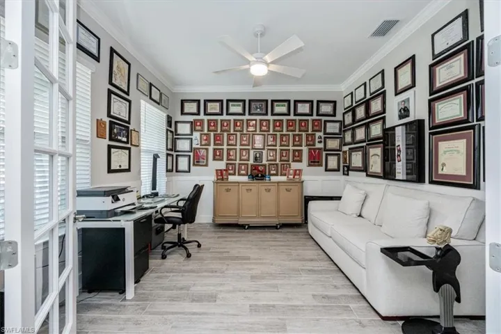 Home office featuring crown molding, light wood-type flooring, a wainscoted wall, a ceiling fan, and a decorative wall