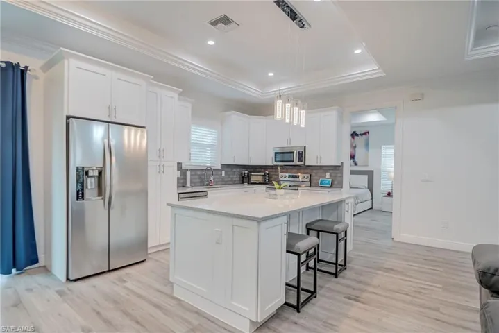 Kitchen with stainless steel appliances, ornamental molding, white cabinetry, light wood-type flooring, and pendant lighting