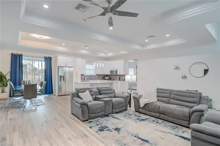 Living area featuring a tray ceiling, ornamental molding, light wood-type flooring, ceiling fan, and recessed lighting