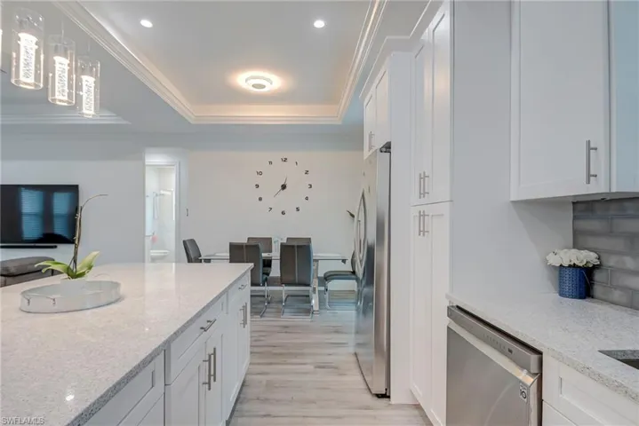 Kitchen featuring white cabinets, light stone countertops, stainless steel appliances, light wood-style floors, and a raised ceiling