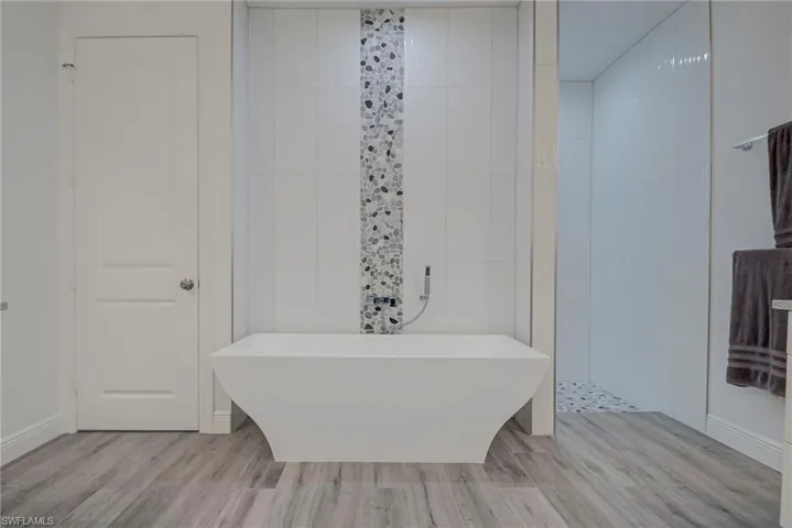 Bathroom featuring a freestanding tub, wood finished floors, tile walls, and a walk in shower