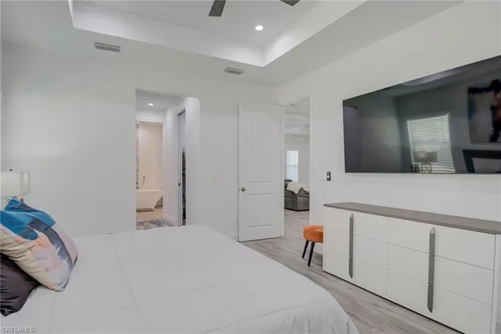 Bedroom featuring light wood-style flooring, a tray ceiling, ceiling fan, ensuite bathroom, and recessed lighting