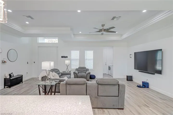 Living room featuring light wood-type flooring, ornamental molding, a ceiling fan, a tray ceiling, and recessed lighting