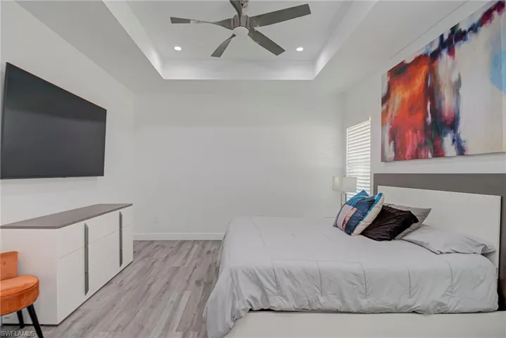 Bedroom featuring a raised ceiling, light wood finished floors, a ceiling fan, and recessed lighting