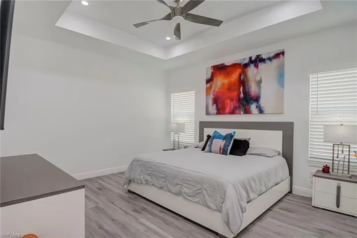 Bedroom featuring a tray ceiling, light wood-style flooring, a ceiling fan, and recessed lighting