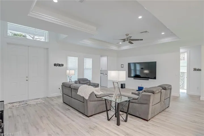 Living room with a ceiling fan, a tray ceiling, crown molding, light wood-style floors, and recessed lighting