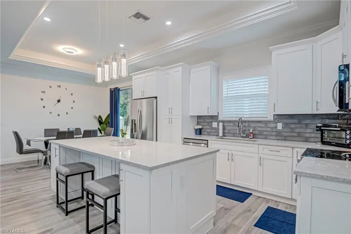 Kitchen featuring white cabinets, ornamental molding, a breakfast bar area, backsplash, and a raised ceiling