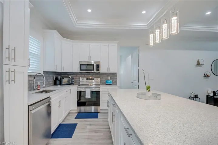 Kitchen with stainless steel appliances, white cabinets, light stone countertops, decorative backsplash, and a raised ceiling