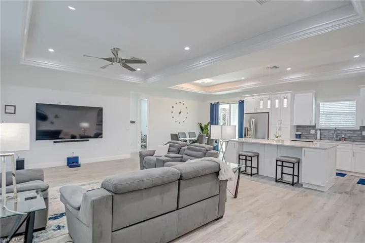 Living room featuring crown molding, ceiling fan, light wood-type flooring, a tray ceiling, and recessed lighting