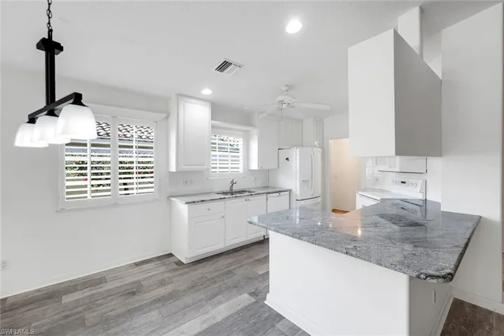 Kitchen with a peninsula, light stone countertops, white appliances, light wood-style floors, and white cabinetry