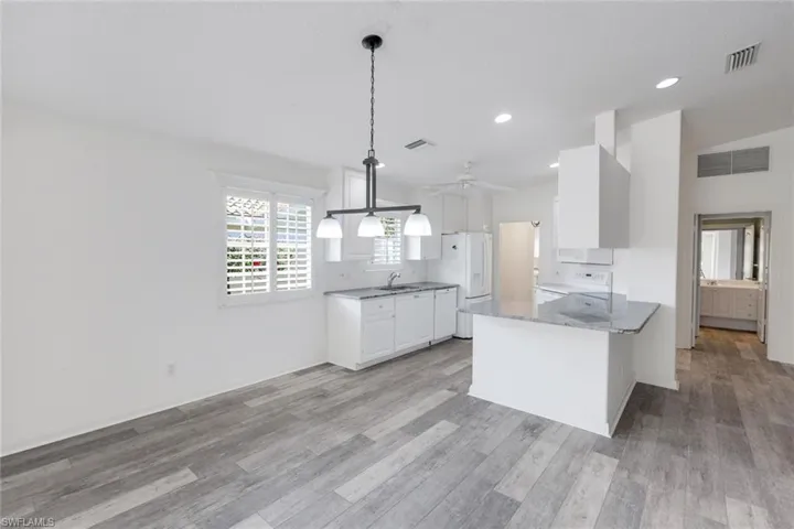 Kitchen featuring a peninsula, white cabinetry, light stone counters, lofted ceiling, and light wood-style flooring