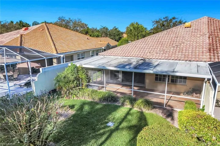 Back of house with a sunroom, glass enclosure, a tiled roof, and a lawn