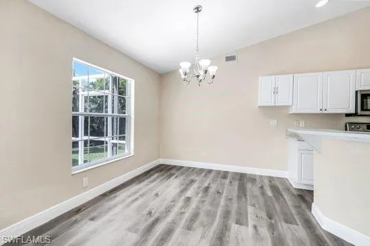 Unfurnished dining area featuring a healthy amount of sunlight, an inviting chandelier, and light hardwood / wood-style floors