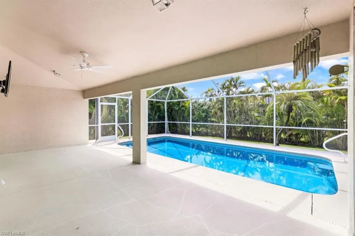 View of pool with glass enclosure, ceiling fan, and a patio