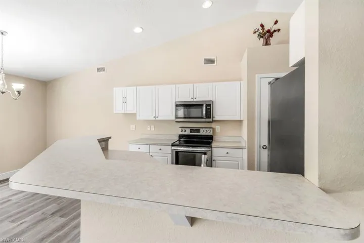 Kitchen with decorative light fixtures, stainless steel appliances, kitchen peninsula, white cabinetry, and a chandelier