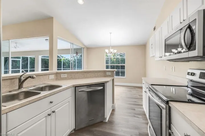 Kitchen with hanging light fixtures, appliances with stainless steel finishes, light hardwood / wood-style floors, white cabinetry, and sink