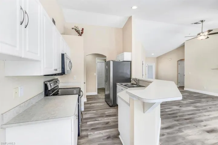 Kitchen featuring a kitchen breakfast bar, hardwood / wood-style floors, appliances with stainless steel finishes, ceiling fan, and white cabinets