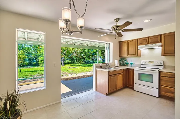 Kitchen featuring white range with electric stovetop, pendant lighting, brown cabinets, light countertops, and light tile patterned floors