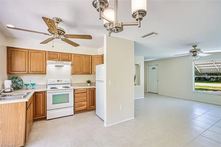 Kitchen featuring a ceiling fan, white appliances, light countertops, and brown cabinets