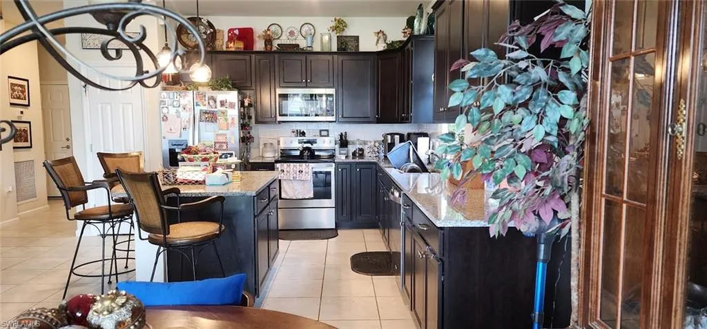 Kitchen with appliances with stainless steel finishes, light tile patterned floors, light stone counters, and a kitchen island