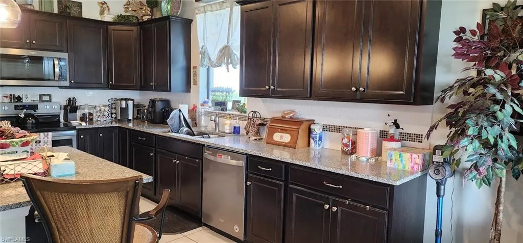 Kitchen featuring stainless steel appliances, light stone counters, dark brown cabinetry, and backsplash