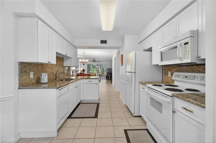 Well-appointed kitchen features newer white shaker cabinetry, granite countertops and backsplash, and tile floors