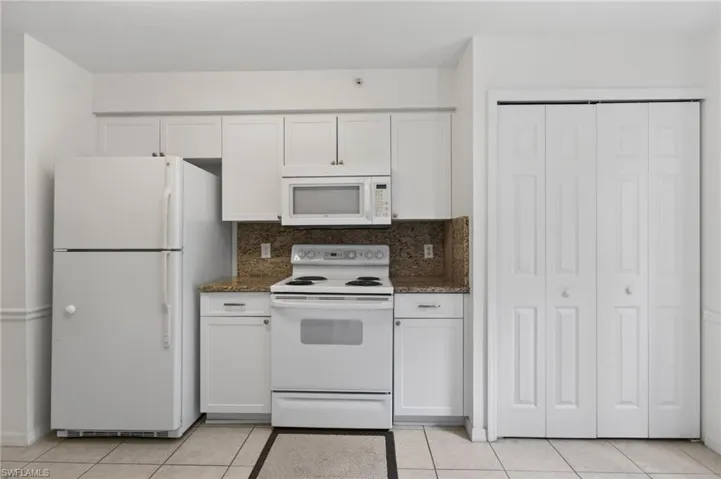 The kitchen features white cabinetry, a refrigerator, an oven with a stovetop, and a microwave