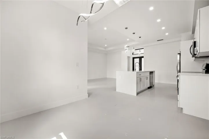 Kitchen featuring white cabinets, an island with sink, stainless steel appliances, hanging light fixtures, and a tray ceiling