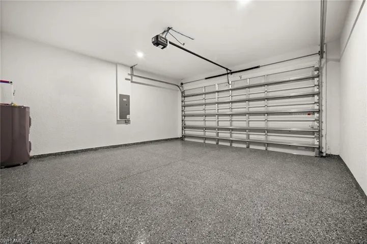Garage featuring electric water heater, electric panel, and a garage door opener