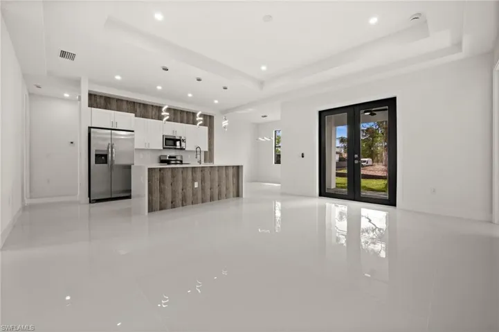 Kitchen with stainless steel appliances, french doors, an island with sink, open floor plan, and hanging light fixtures