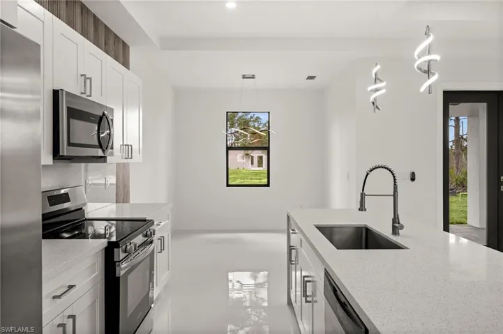 Kitchen with stainless steel appliances, white cabinetry, light stone counters, and decorative light fixtures