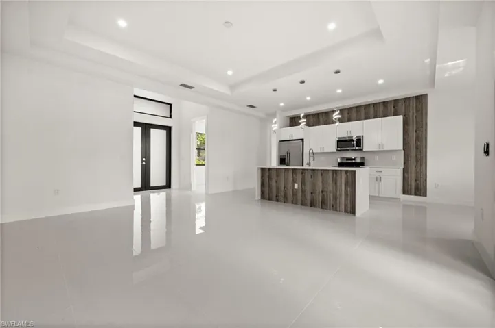 Unfurnished living room with french doors, a raised ceiling, light tile patterned floors, and recessed lighting
