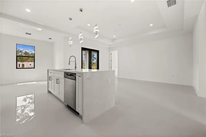Kitchen with a kitchen island with sink, light stone counters, healthy amount of natural light, white cabinetry, and a tray ceiling