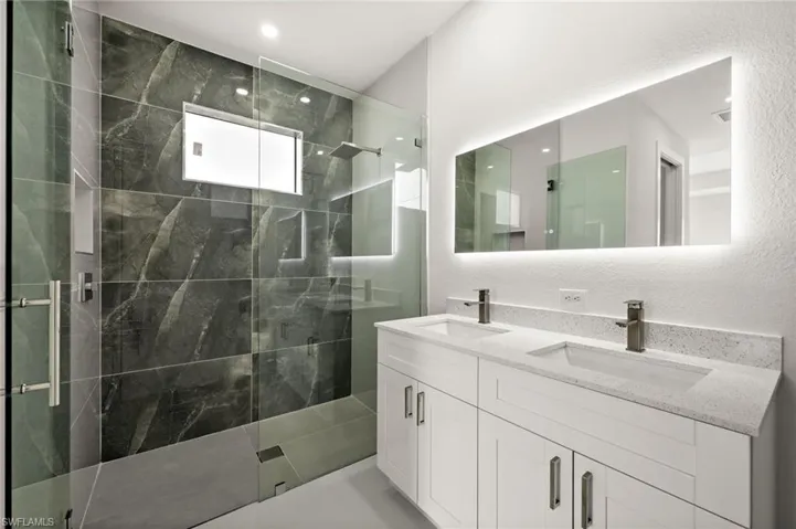 Full bath with a textured wall, a marble finish shower, double vanity, and recessed lighting