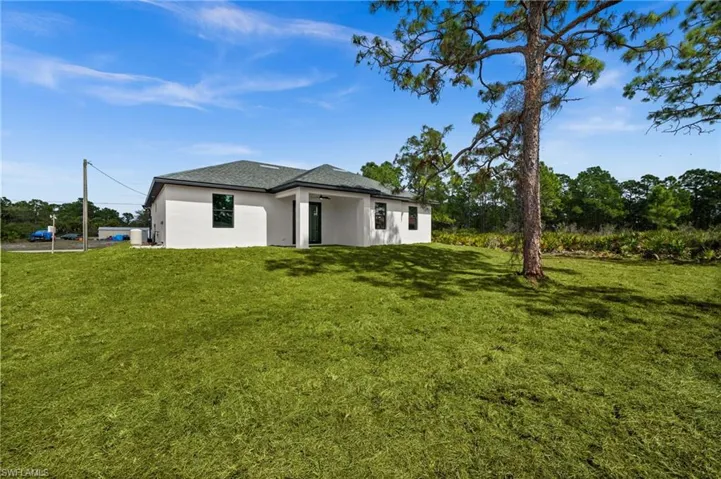 Back of house featuring stucco siding, a yard, and a shingled roof