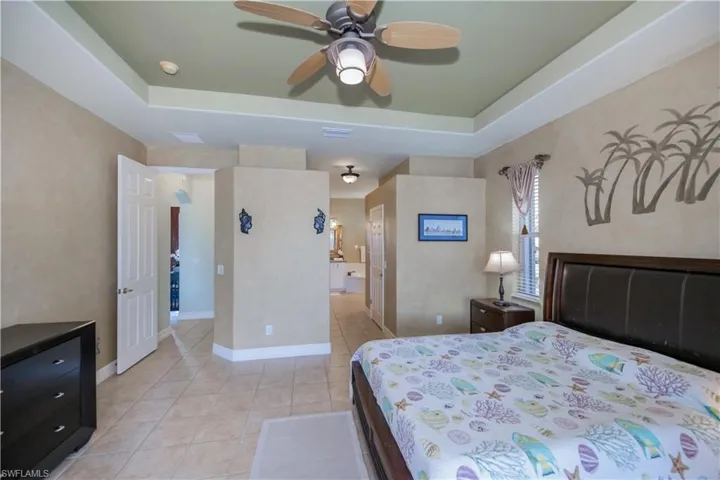 Bedroom featuring light tile patterned floors, a tray ceiling, ensuite bathroom, and a ceiling fan