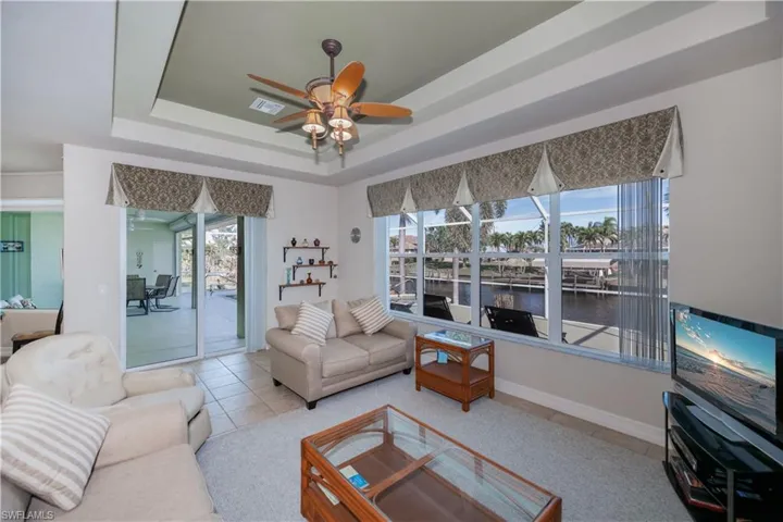 Tiled living room featuring a tray ceiling, plenty of natural light, ceiling fan, and a sunroom