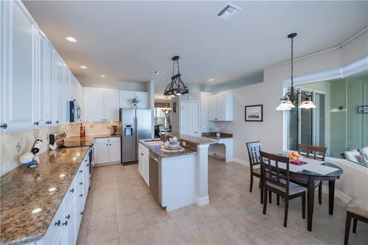 Kitchen with decorative backsplash, appliances with stainless steel finishes, a chandelier, a kitchen island with sink, and stone counters